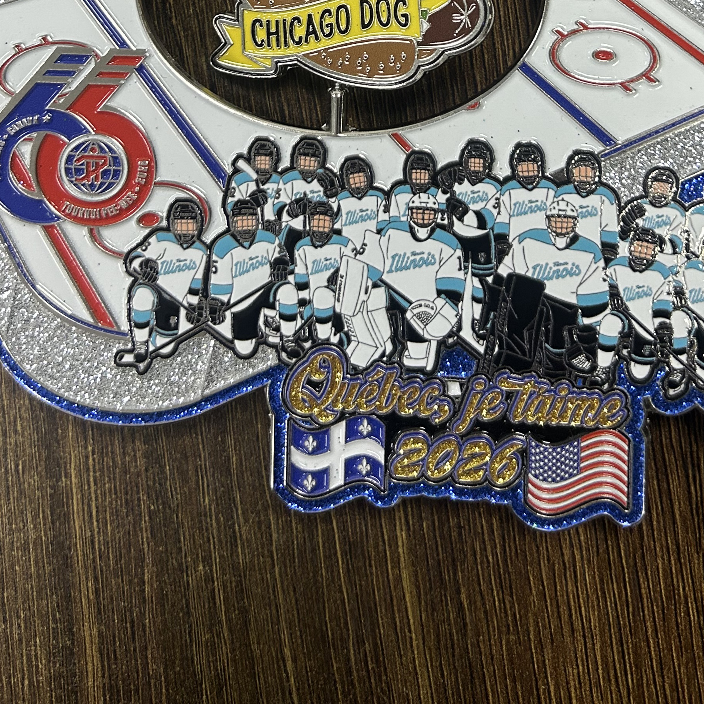 Close documentary photograph of a manufactured hockey trading pin showing glitter enamel, raised metal, a moving food-shaped spinner, illustrated players, rink markings, and event lettering.
